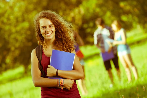 Jonge vrouwelijke student in het park met andere vrienden — Stockfoto