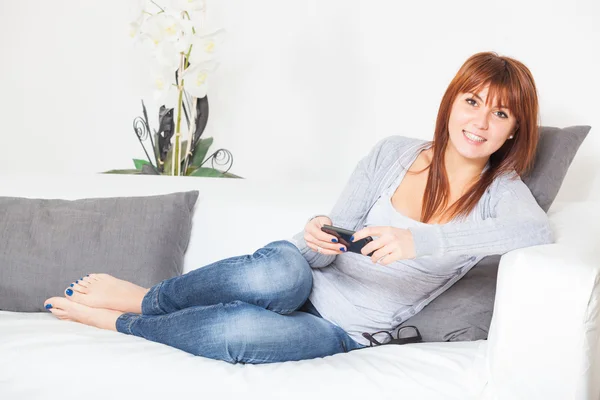 Schöne junge Frau mit Smartphone auf dem Sofa — Stockfoto