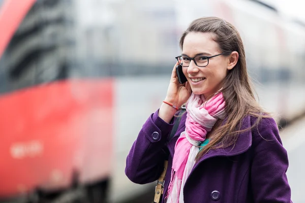 Ung kvinna talar på mobilen vid järnvägsstationen — Stockfoto