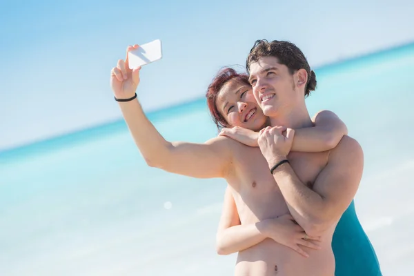 Pareja joven tomando autorretrato con móvil en la playa — Foto de Stock