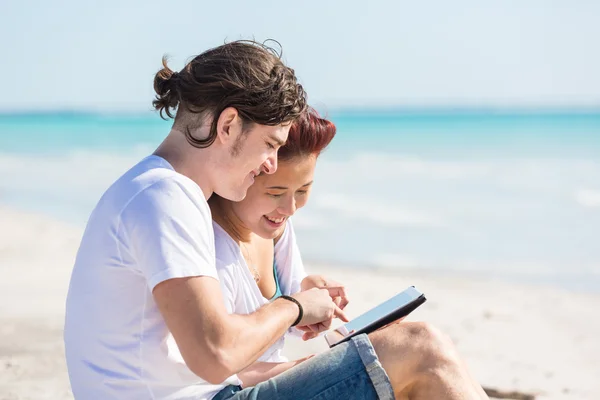 Pareja joven en la playa con tableta digital — Foto de Stock