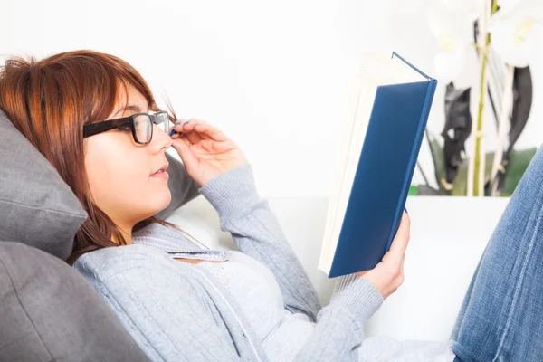 Schöne junge Frau mit einem Buch auf dem Sofa — Stockfoto