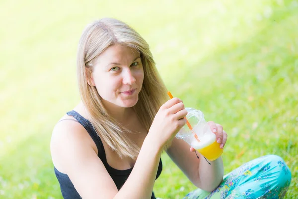 金髪の女性が公園でフルーツ ジュースを飲む — ストック写真