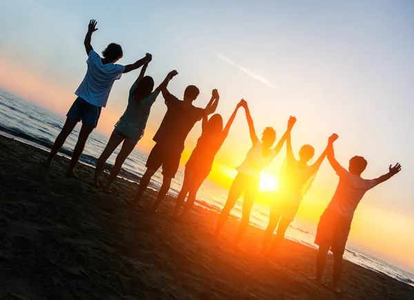 Groep mensen met opgeheven armen op zoek bij zonsondergang — Stockfoto