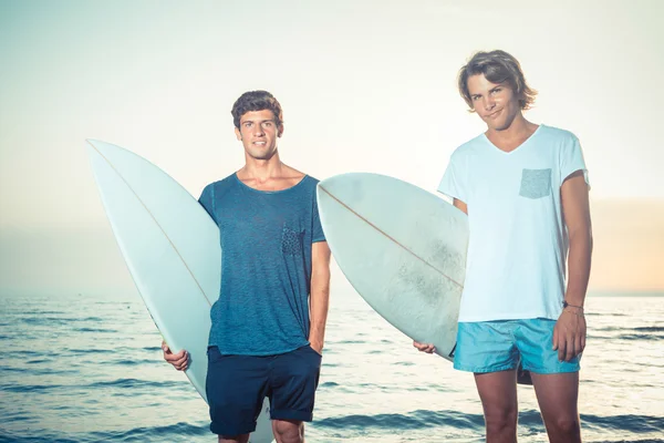Dwóch chłopców z deski surfingowe na zachodzie słońca — Zdjęcie stockowe