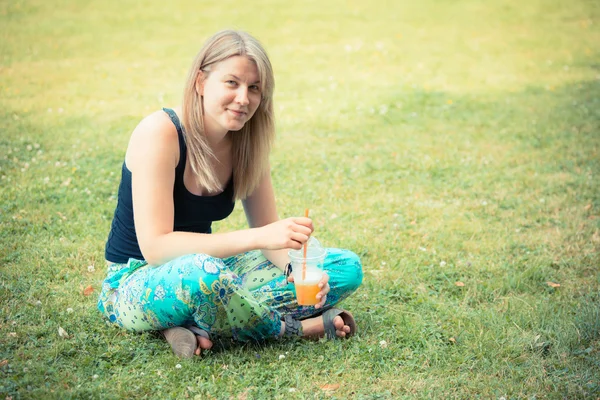 Mujer rubia bebiendo jugo de fruta en el parque —  Fotos de Stock