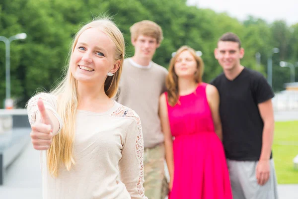 Meisje met Duimschroef opwaarts en vrienden op achtergrond — Stockfoto