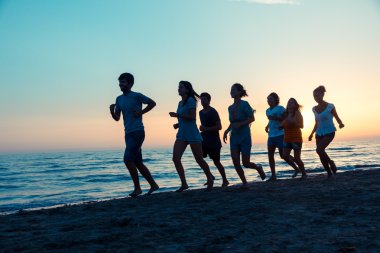 Gün batımında sahilde koşan bir grup insan.
