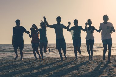 Gün batımında sahilde koşan bir grup insan.