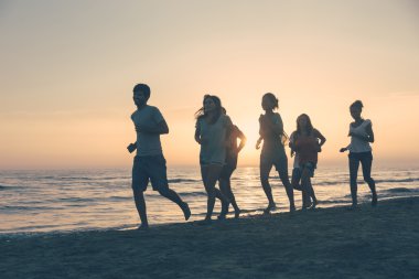 Gün batımında sahilde koşan bir grup insan.