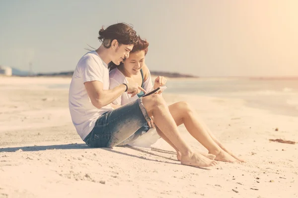 Pareja joven en la playa con tableta digital —  Fotos de Stock
