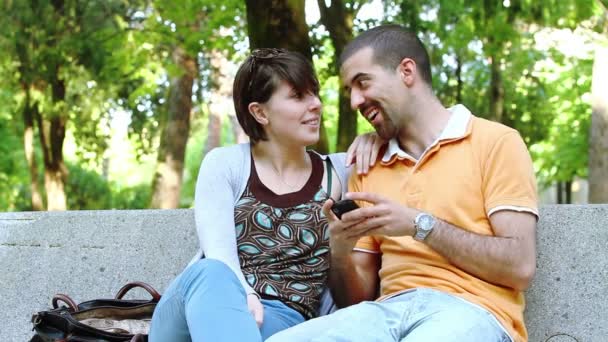 Hombre y mujer en el parque mirando teléfono móvil — Vídeo de stock