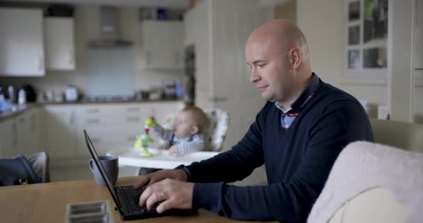 Молодий батько працює з дому і грає зі своїм новонародженим хлопчиком в — стокове відео