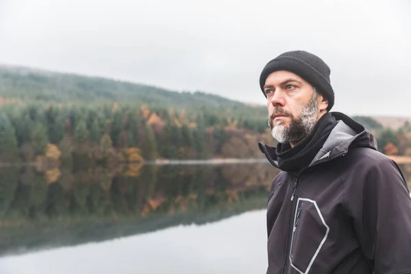 秋天户外留胡子的男人 穿着保暖衣服 头戴羊毛帽 站在湖边远眺的成年人 秋天风格的肖像 — 图库照片