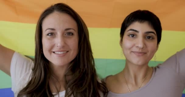 Gelukkig meisje vrienden lesbisch paar holding een trots regenboog vlag op achtergrond — Stockvideo