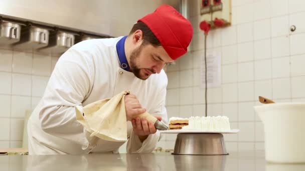Cukiernik w pracy w cukierni przygotowujący i ozdabiający ciasto bitą śmietaną — Wideo stockowe