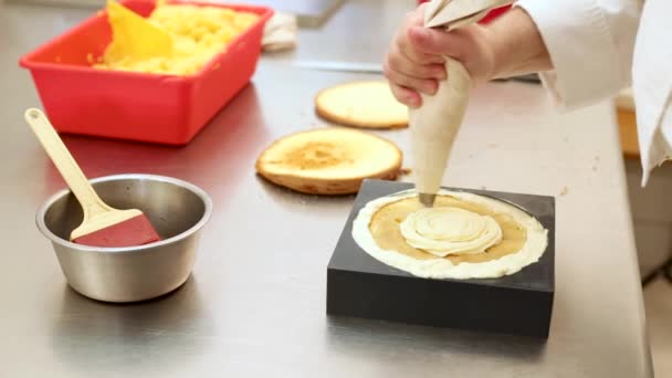 Bir restoranın mutfağında pasta şefi kremayla tatlı bir pasta süslüyor. — Stok video