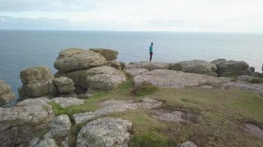 Cornwall 'da uçurumun tepesindeki adam manzaranın tadını çıkarıyor.