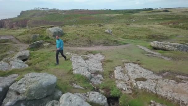 Egy ember egy sziklán Cornwallban élvezi a kilátást. — Stock videók