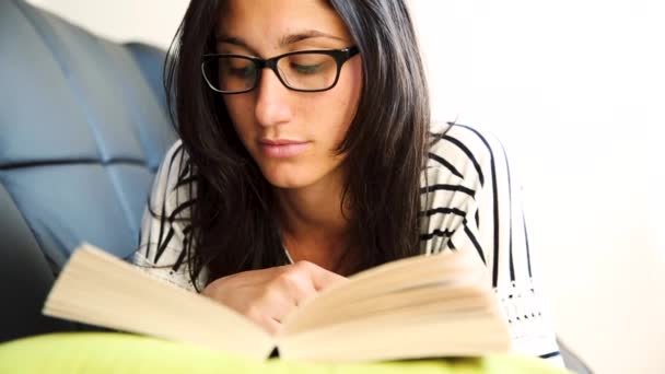 Mujer joven relajándose y leyendo un libro en el sofá — Vídeos de Stock