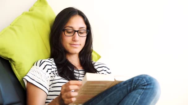 Mujer joven relajándose y leyendo un libro en el sofá — Vídeos de Stock