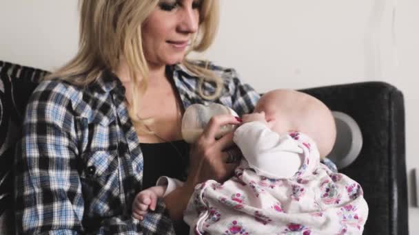 Mãe alimentando sua menina com mamadeira de leite no sofá — Vídeo de Stock