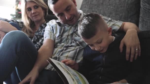 Padres ayudando a su hijo a leer un libro y hacer la tarea escolar — Vídeos de Stock