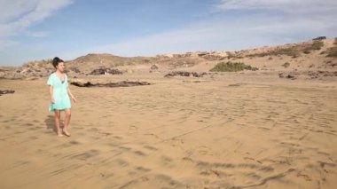Güzel bir kadın sahilde kumsalda yürüyor ve arkasında ayak izleri bırakıyor.