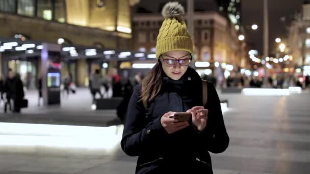 Autentisk bild av kvinna med hjälp av smarttelefon i staden på natten i London — Stockvideo