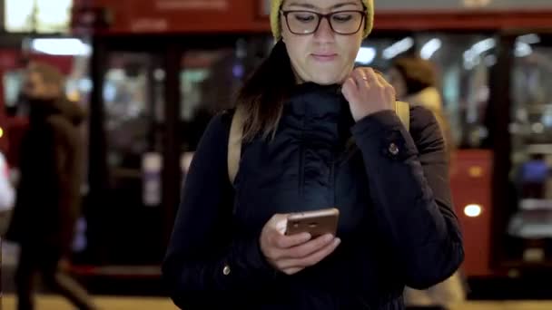 Autentisk bild av kvinna med hjälp av smarttelefon i staden på natten i London — Stockvideo