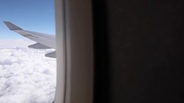 Airplane flying above clouds with a blue sky over the horizon, over wing window view - High altitude flying while cruising on a long haul flight - Transportation and travel concepts
