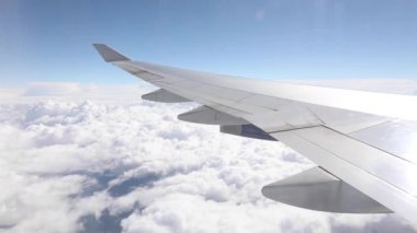 Airplane flying above clouds with a blue sky over the horizon, over wing window view - High altitude flying while cruising on a long haul flight - Transportation and travel concepts