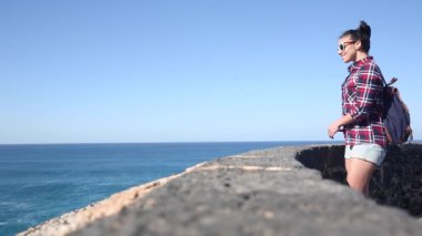 Happy young woman at seaside enjoying the view of the ocean and taking photos on a sunny day in Fuerteventura - Travel and lifestyle concepts