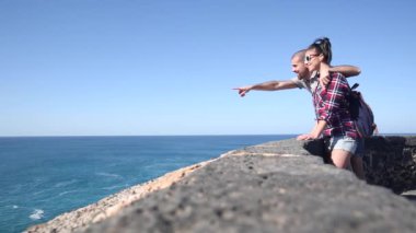 Authentic shot of a young couple at seaside enjoying the view of the ocean and some nice time together on a sunny day in Fuerteventura - Travel and lifestyle concepts