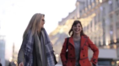Authentic slow motion shot of two happy female friends enjoying shopping time together in London, talking, smiling and laughing while walking in the city