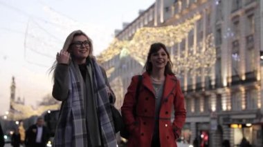 Authentic slow motion shot of two happy female friends enjoying shopping time together in London, talking, smiling and laughing while walking in the city