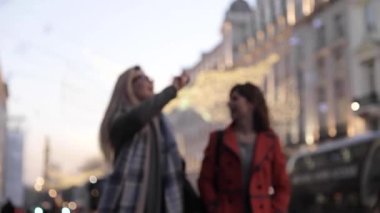 Authentic slow motion shot of two happy female friends enjoying shopping time together in London, talking, smiling and laughing while walking in the city
