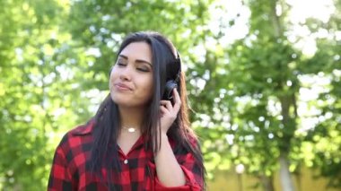 Authentic shot portrait of a beautiful mixed race asian girl with headphones to listen to music at park on a sunny summer day with green trees on background
