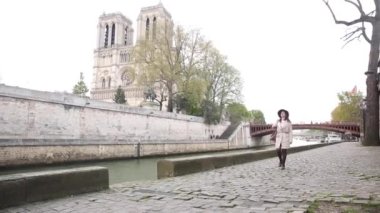 Bulutlu bir günde Notre Dame katedrali ile Paris 'te Seine nehri boyunca yürüyen mutlu bir kadının otantik çekimi.