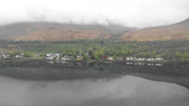 Aerial view of lakes and green landscape in Scotland and a little village on the lake edge with reflections on the water on a cloudy day in the highlands