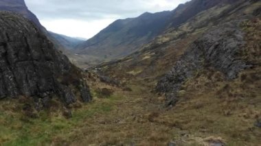 Aerial view of a valley in the Highlands with a road that winds through the mountains in the northern Scotland on a cloudy moody day for travel and lanscape concepts