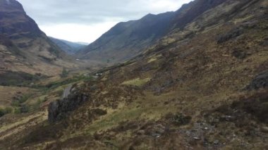 Aerial view of a valley in the Highlands with a road that winds through the mountains in the northern Scotland on a cloudy moody day for travel and lanscape concepts