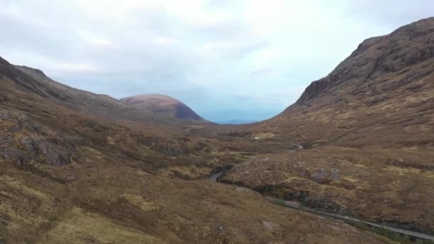 ハイランド地方の渓谷を空中から眺め 北スコットランドの山々を旅や風景のコンセプトのために曇った気分の日に風が吹く道路 — ストック動画