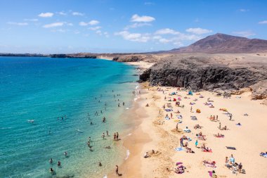 LANZAROTE, SPAIN - June 30, 2022: People at seaside enjoying crystal clear water and white sand on a sunny day