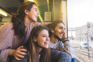 Mutlu bir arkadaş grubu, güneşli bir günde Portekiz 'de tatilde birlikte seyahat ederken trenden dışarı bakıyor. Gülümseyen genç adam ve kadınlar, sağda kopya alanı.