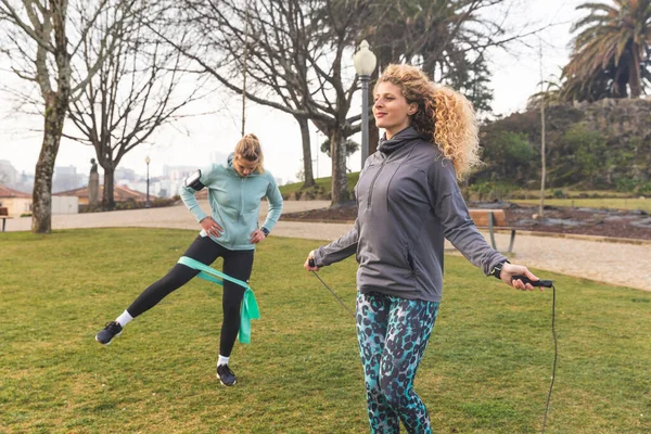 Women doing work out at park, jumping rope and strenght exercises - two beautiful young women in Porto training together on a cloudy day - outdoor activities and sport