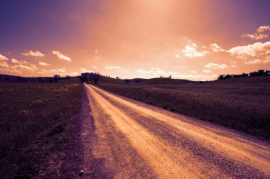 Gün batımında Toskana bahar tarlaları arasında dönen toprak yol..