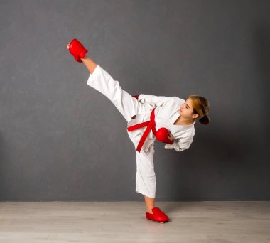 Beyaz kimonolu ve kırmızı elbiseli genç bir Karateka kızı gri bir duvara karşı antrenman yapıyor.