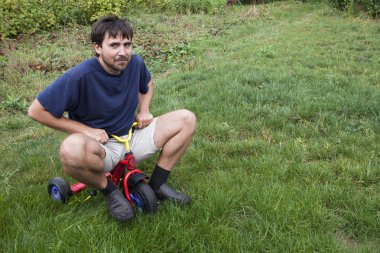 küçük bir üç tekerlekli bisiklet üzerinde yetişkin erkek
