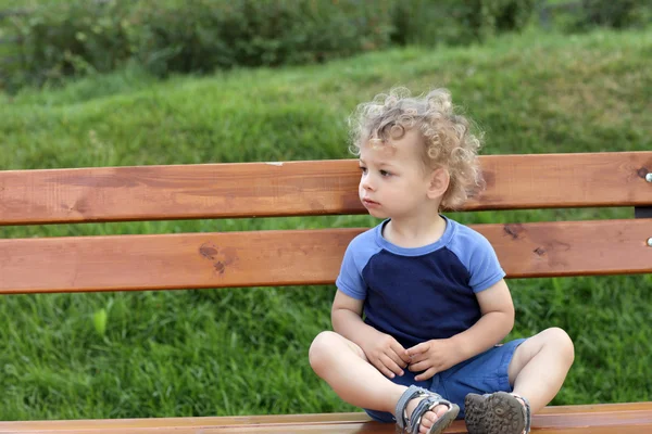 Кудрявый ребенок на скамейке — стоковое фото